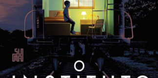 Recorte da capa do livro. Imagem de um ambiente noturno, da parte de tras de um vagão de trem sobre trilhos, no lugar da parede de tras do vagão está um quarto de um garoto, com ele sentado na cama, uma mesa cadeira, abajur e uma janela para um céu claro. Em primeiro plano, abaixo, o título: "O Instituto".