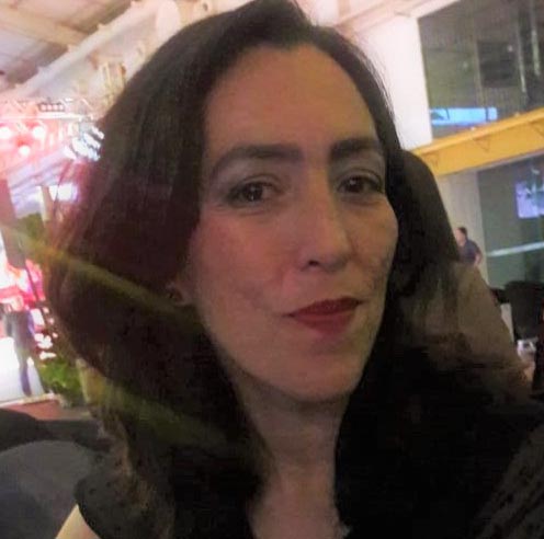 Camila Vieira, olhando para a câmera, com batom vermelho e cabelos longos e escuro