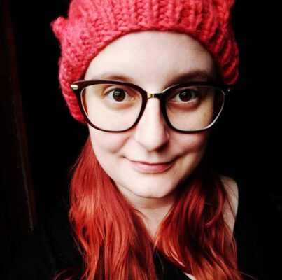 Nicole, usando óculos e uma touca vermelha, e cabelos vermelhos