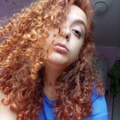 Adriana Adriana, com blusa azul, cabelo castanho, longo, ondulado cobrindo metade do rosto