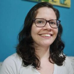 Carol Vidal Carol Vidal, sorridente, de roupa branca, óculos e olhando para frente