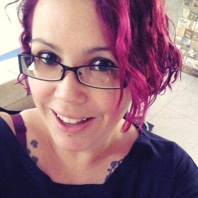 Selfie de Domenica Mendes, sorridente, de óculos roupa escura, e cabelo roxo