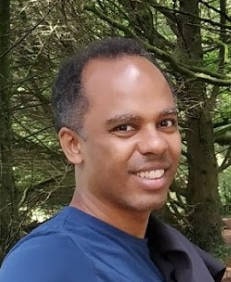 Hamilton Kabuna, sorridente, com camiseta azul, e com árvores no fundo.