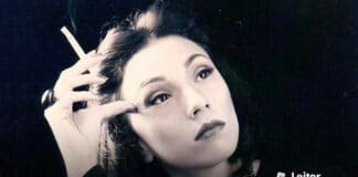 Foto de rosto de Clarice Lispector, em um fundo escuro. Ela olha para o lado, com a cabeça inclinada e apoiada sobre um dedo, e segurando um cigarro nessa mesma mão.