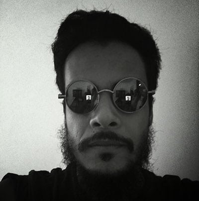 Foto preto e branca de rosto de Rodrigo. com semblante sério, e oculos refletindo o ambiente