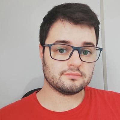 Selfie de Guilherme de Biasi. Homem branco, com cabelo e barba castanha. Está usando óculos e vestindo uma camiseta vermelha.