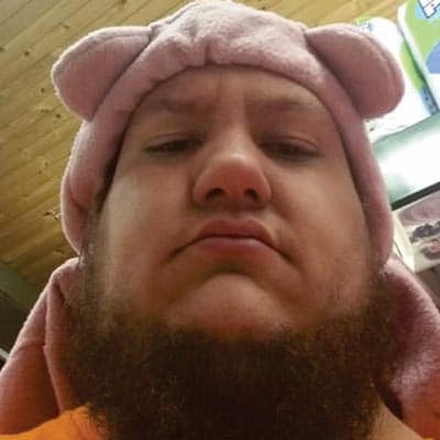 Selfie de Peu Lausi. Homem branco, com barba castanha. Está usando um gorro rosa com orelhas de urso e vestindo uma camiseta laranja.