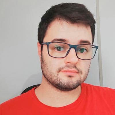 Homem branco de barba rala, óculos azul cabelo preto e camisa vermelha