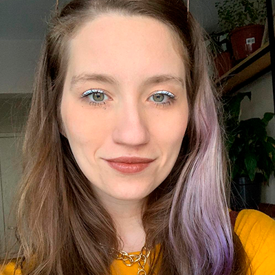 Mulher branca com cabelos loiros e uma mecha turquesa do lado esquerdo. A maquiagem combinando com a cor dos cabelos.